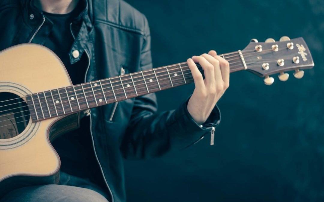 Close-up of a musician playing an acoustic guitar, wearing a leather jacket.