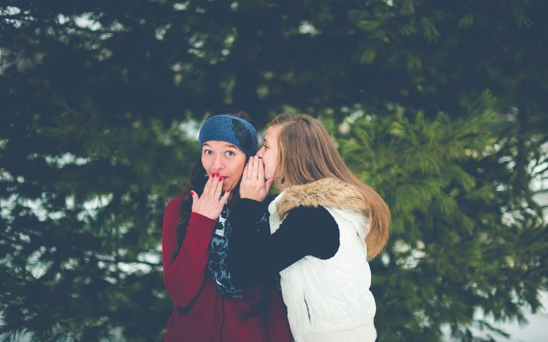 woman whispering on woman's ear while hands on lips