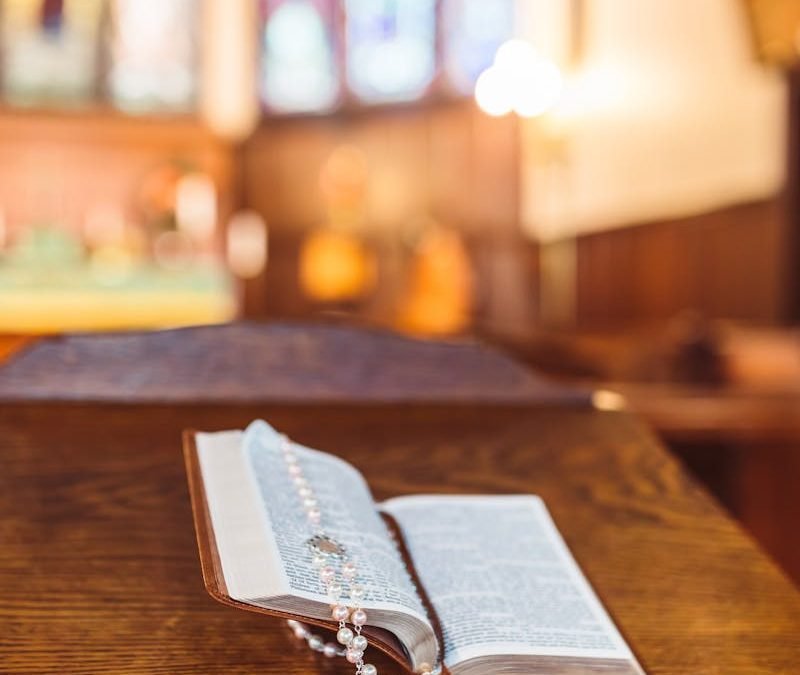 An open Bible with a rosary placed on a wooden altar in a church setting.